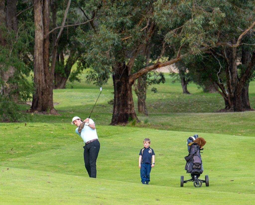 Father-hitting-the-golf-ball-while-his-young-son-is-walking-beside-his-golf-trolley