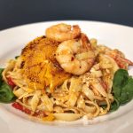 Prawns and pasta on a white plate with spinach and chilies